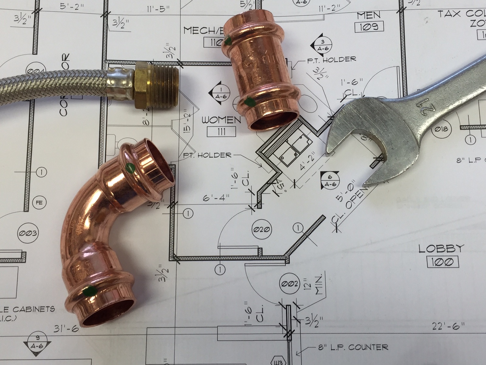 Copper plumbing fittings and a wrench on technical plans